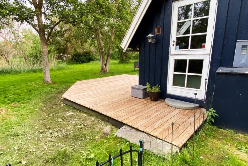 Nærbillede af ubrudte terrassebrædder i brunimprægneret fyr tilpasset facaden og det eksisterende granittrin foran døren i Vordingborg